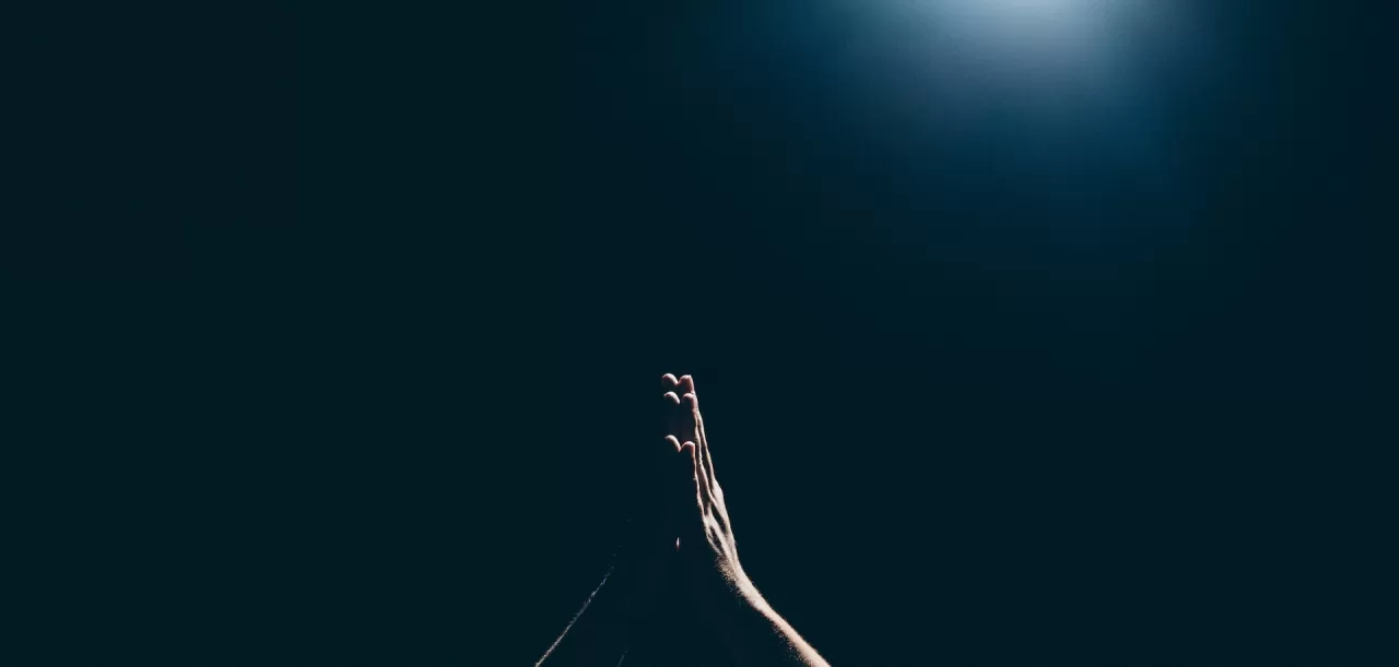 Image of hands praying in dark with overhead light by Amaury Gutierrez on Unsplash
